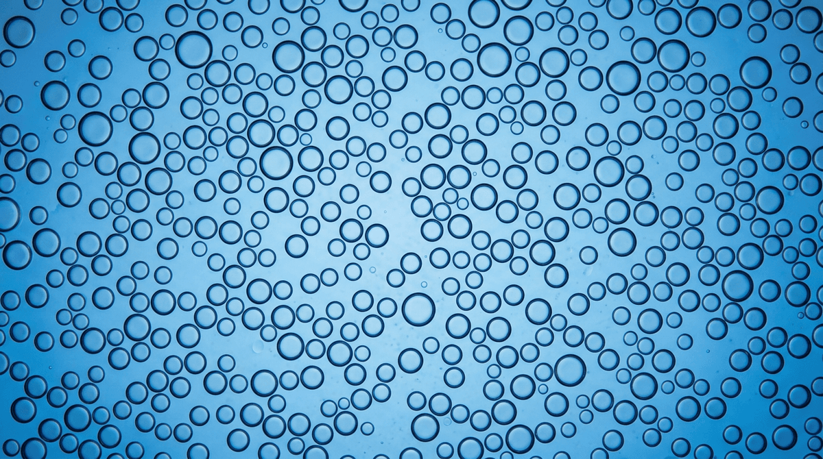 Scientific close-up macro photography of oil-in-water emulsion showing uniform spherical oil droplets dispersed in water phase, microscope view style, blue tinted background, educational illustration